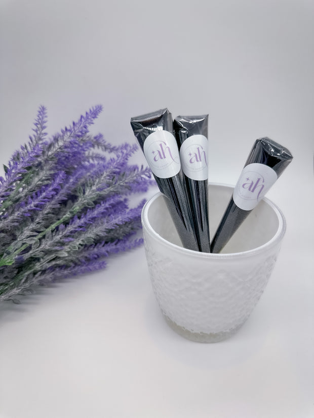 Amarya Henna Jagua cones in a decorative bowl, featuring sleek packaging and rich natural dye for deep blue-black body art. Surrounded by purple rose petals.
