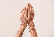 Woman hands featuring intricate deep red henna designs, adorned with bracelets. 