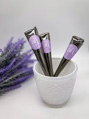 Natural henna cones with purple labels that say 'amarya henna' in white lettering. The cones are in a clear glass bowl with a textured surface. The bowl is surrounded by purple flower petals.