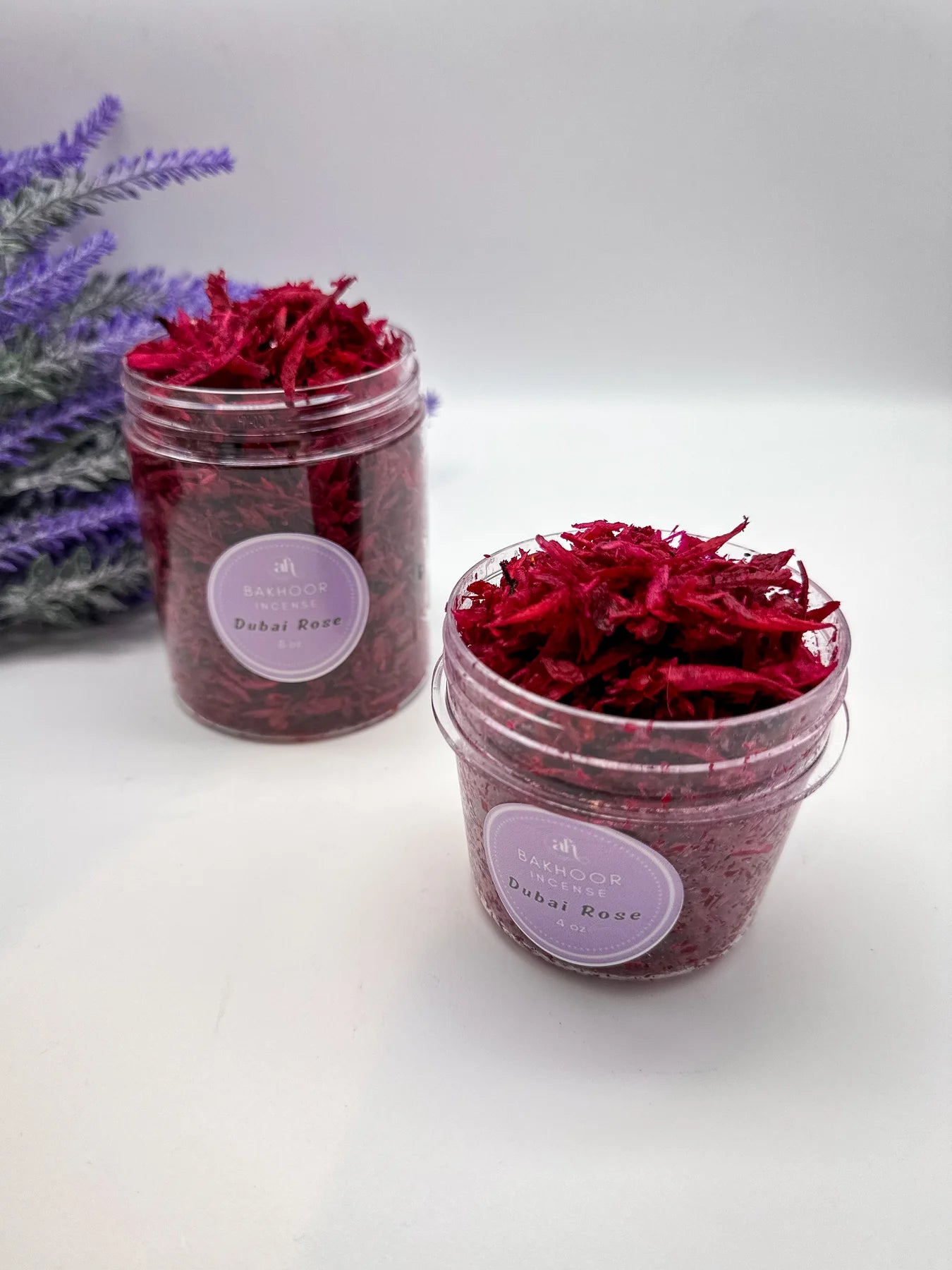 Two jars of red bakhoor incense with lavender flowers in the background on a white surface