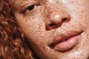 Close-up of a person's face featuring natural-looking henna freckles applied across the nose and cheeks - Shop Amarya Henna products.