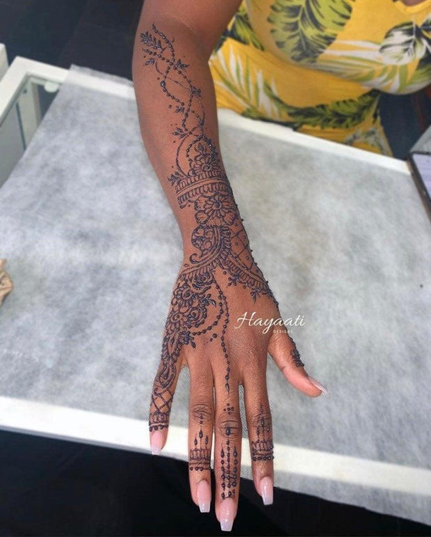 Darker skinned woman hand and arm up to her elbow, adorned with Jagua paste in a dainty design created using Amarya Henna Jagua cones.